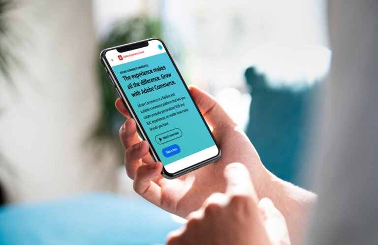 A person holding an iPhone with the Adobe Commerce website on it
