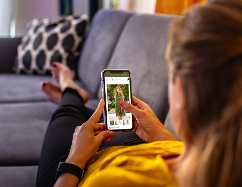 Woman laying on a couch looking at a Jude Connally dress on her iPhone