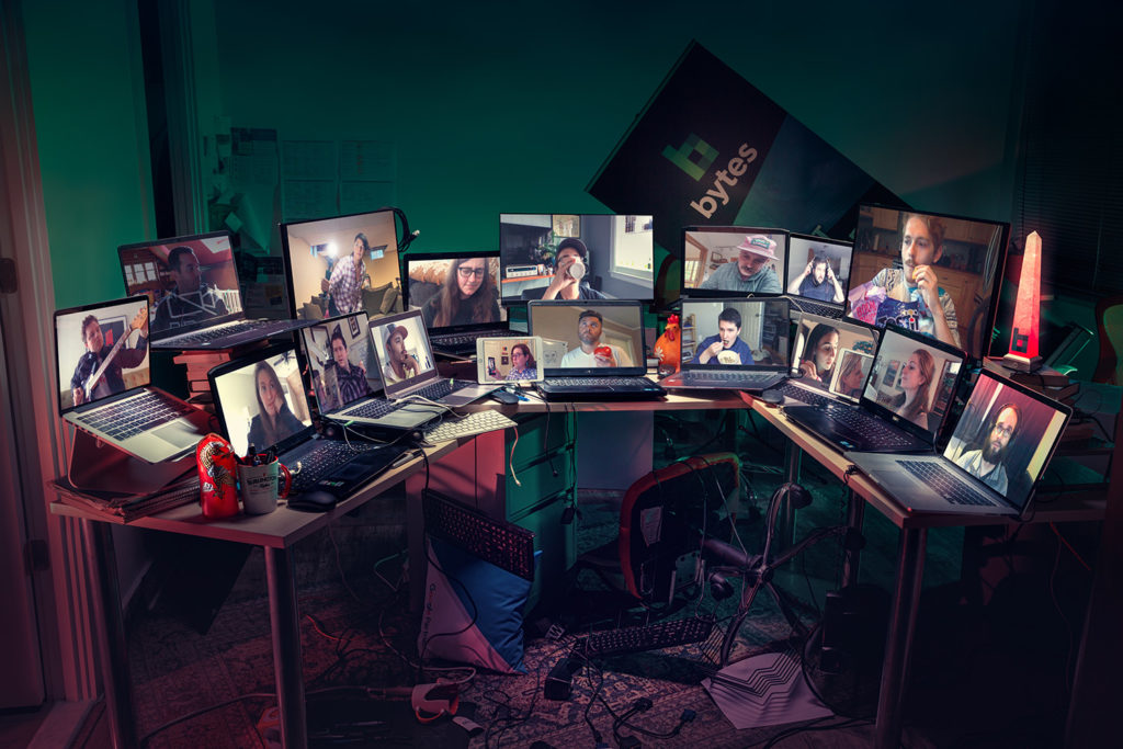 Laptops and desktop computers sit scattered on a table of what looks like an abandoned office; Bytes staff members are all attempting a video call since the workforce is all remote