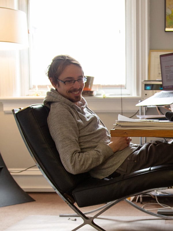 Jay, Pigallevodka.co CEO, is leaning back in his chair at his desk, smiling at someone off camera; office setting, warmly lit by a large window behind him