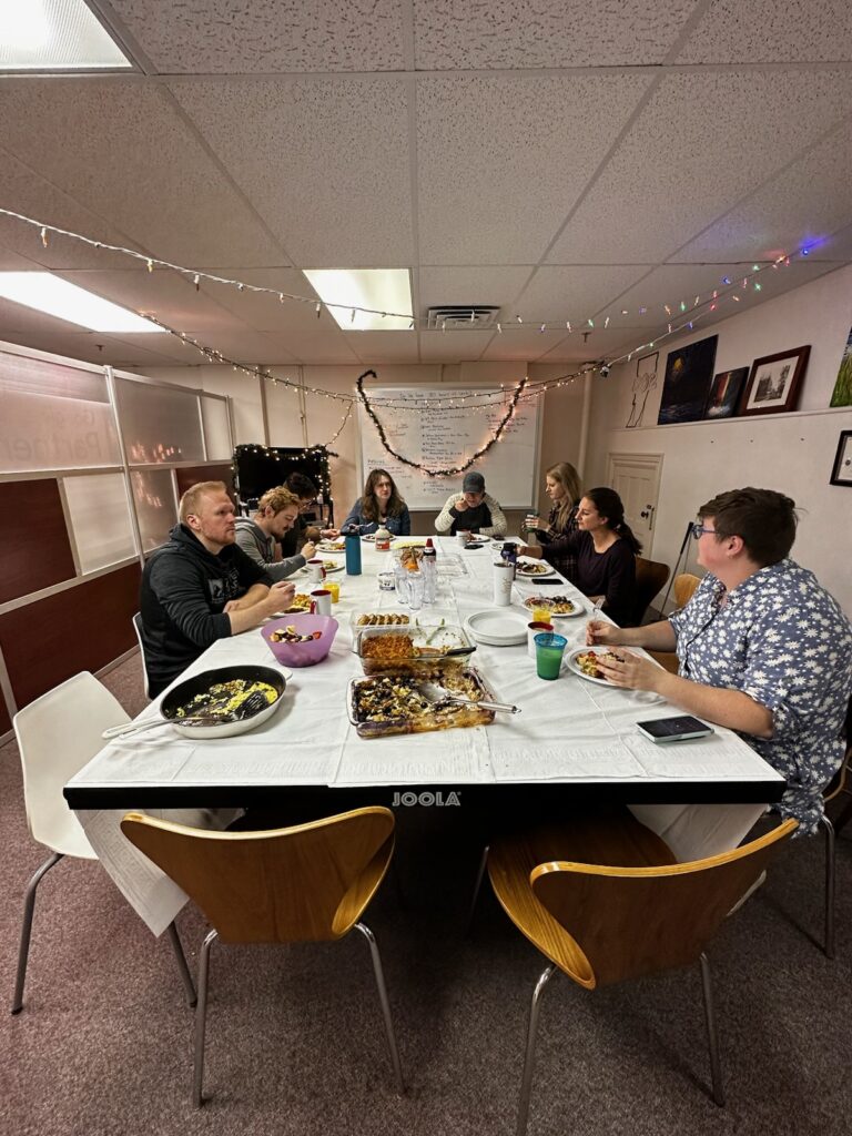 Bytes.co potluck dinner, people sitting around a long table eating food