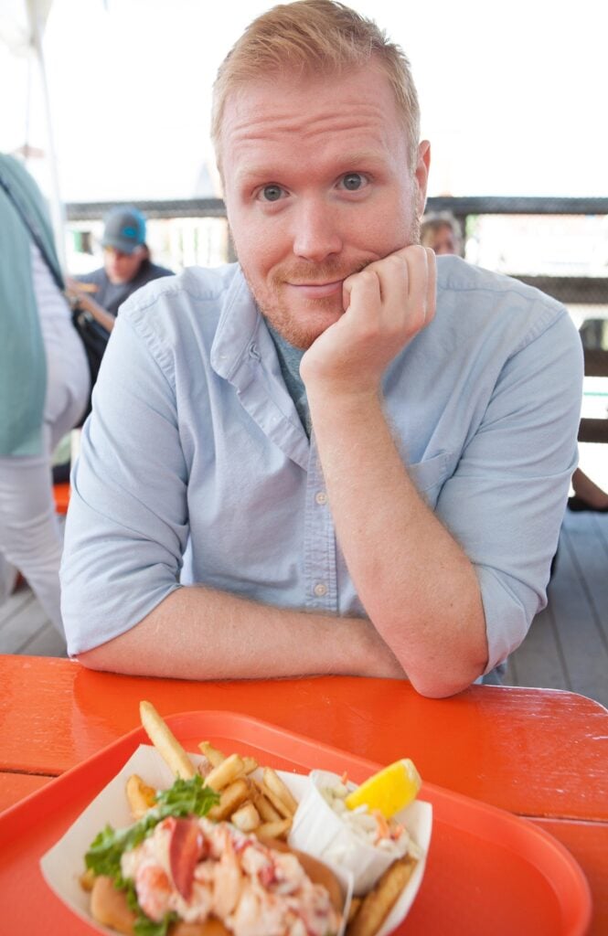 Josh smiling with a lobster roll in a restaurant