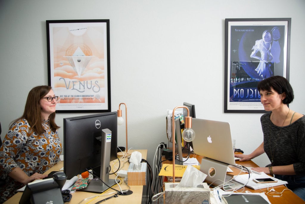 Lilly and Kristina chatting at their desks