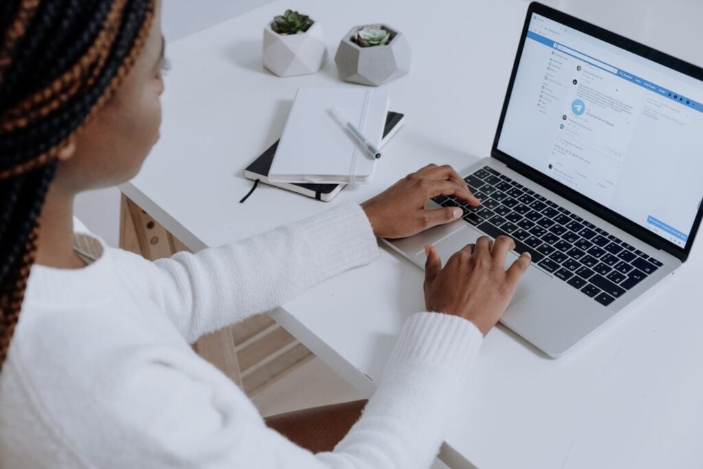 Woman sitting at a white desk using Facebook on her laptop