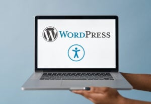 A woman's hands holding a laptop computer with the WordPress and Web Accessibility logos on the screen