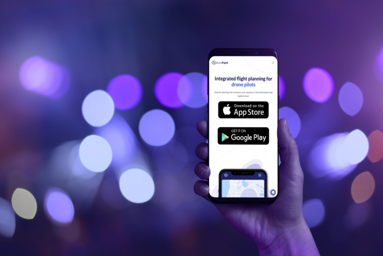 Hand holding a mobile phone with the AutoPylot homepage on its screen. The background behind the hand is full of blurred purple lights.